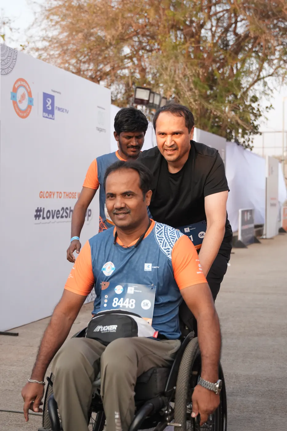 A wheelchair user and his running partner smiling on the course