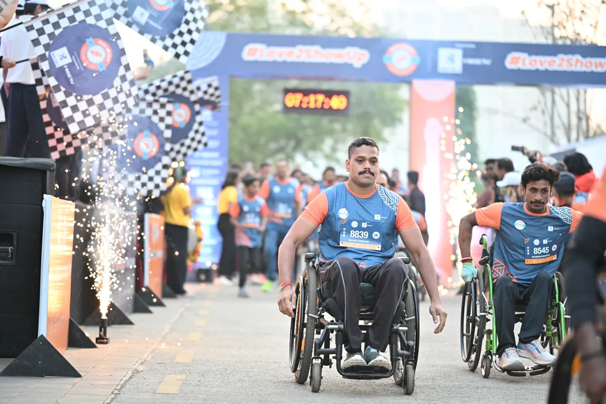 Two wheelchair users crossing the finish arch through fireworks