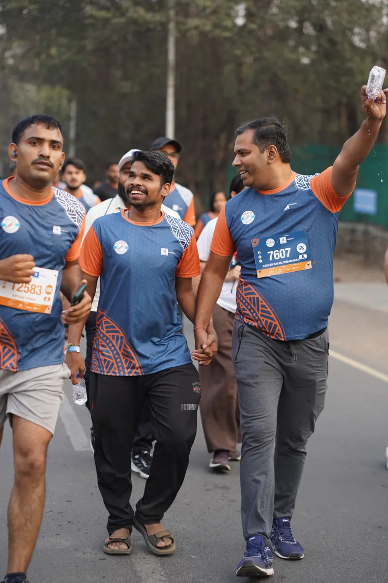 Three friends in Run InSync T-shirts walking and waving on the course