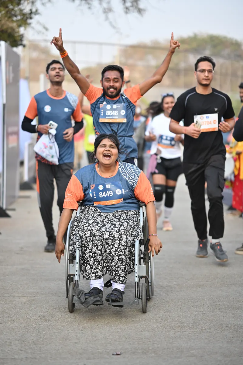A runner in a wheelchair celebrating at the finish with friends cheering behind